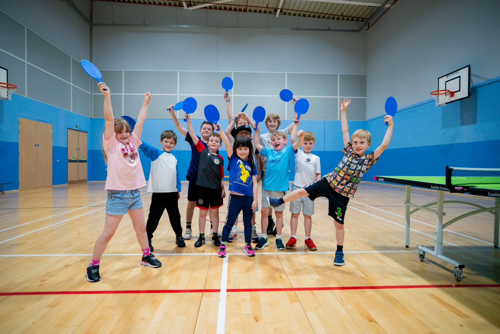 Children cheering with table tennis bats in a sports hall