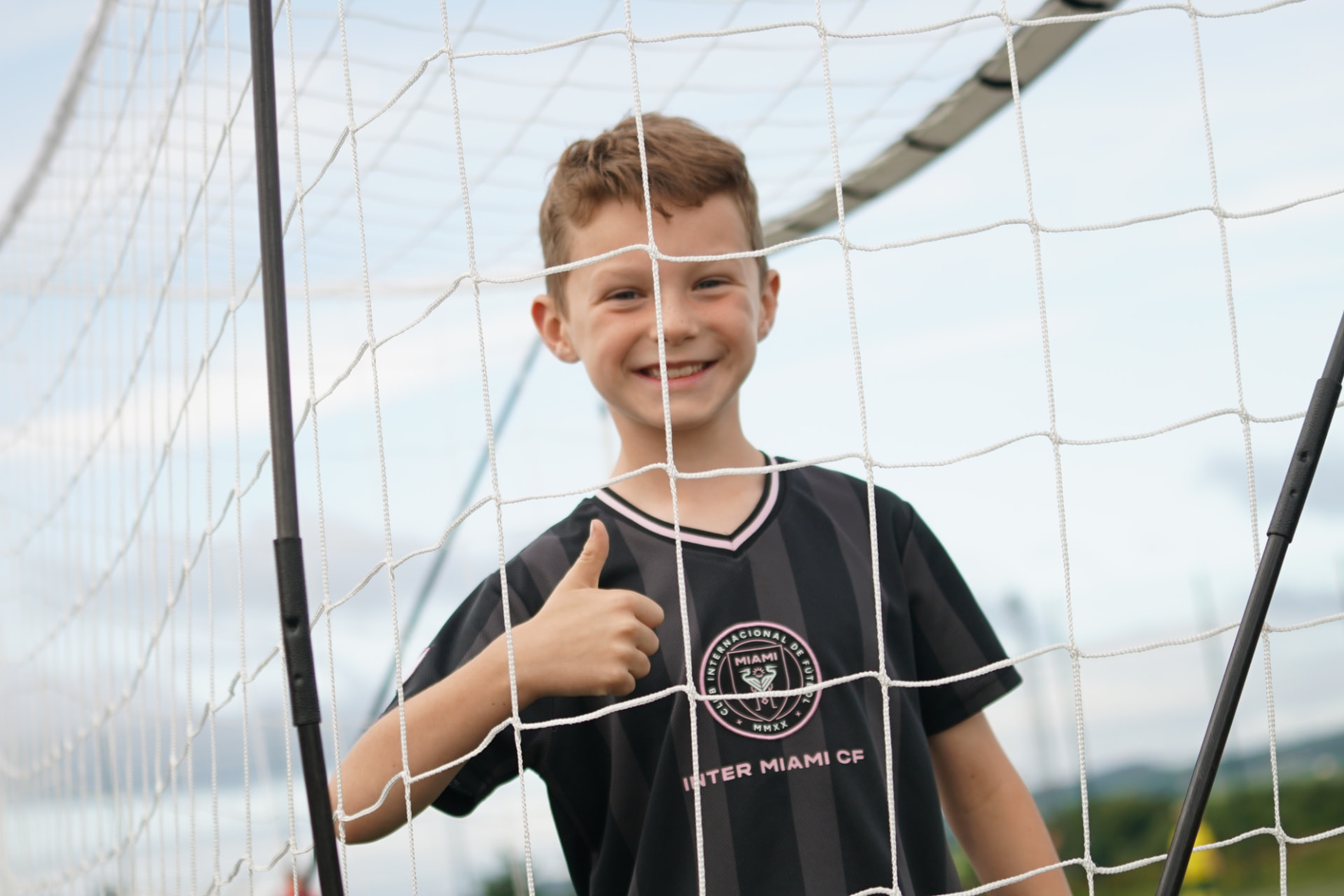 Smiling boy giving a thumbs up behind a football goal net