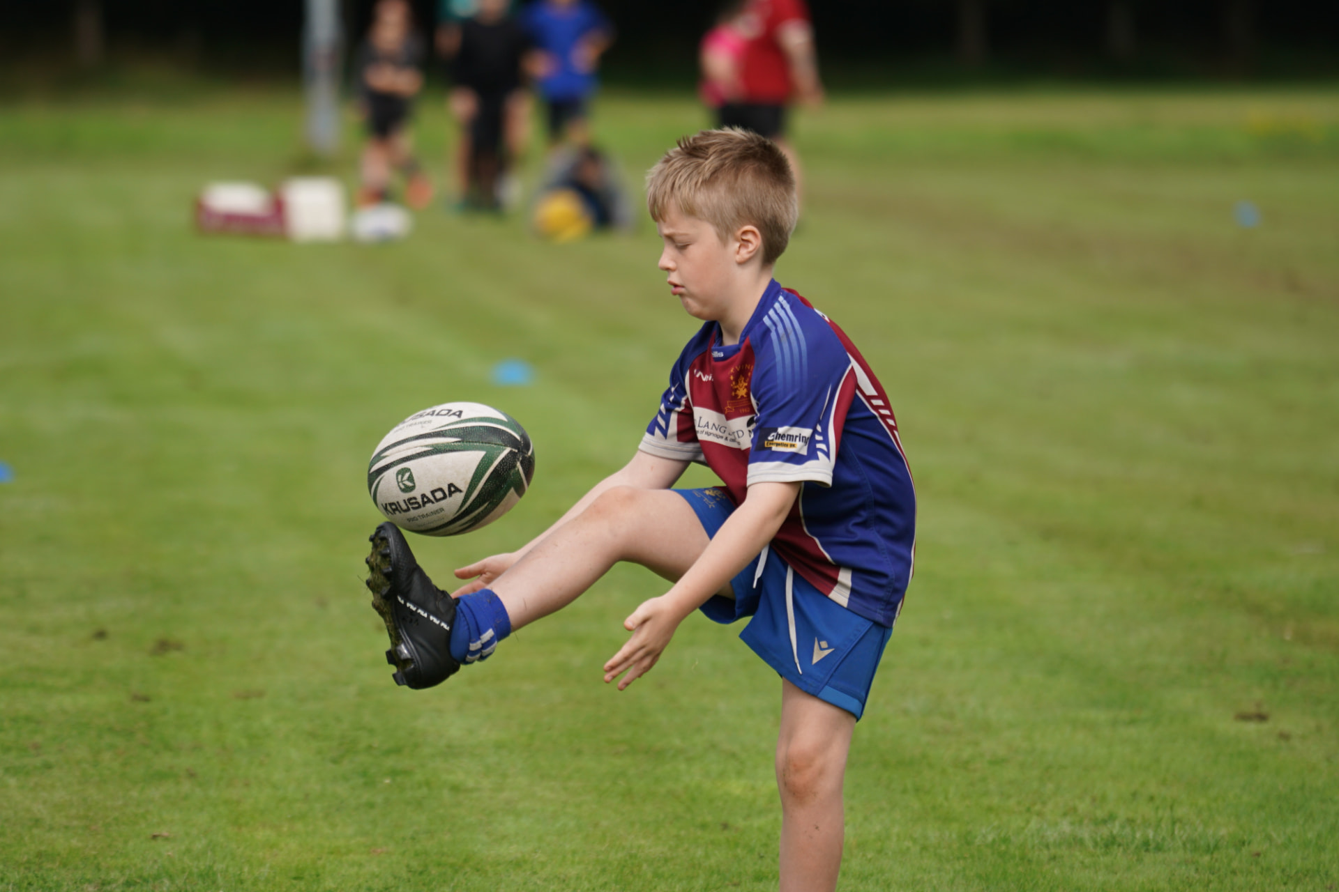 Young rugby player kicking a ball on grass